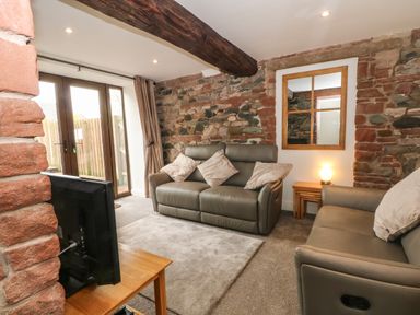 A living room with two grey sofas a television on a wooden stand and a mirror on a stone wall at Saddleback Barn in Newton Reigny near Penrith