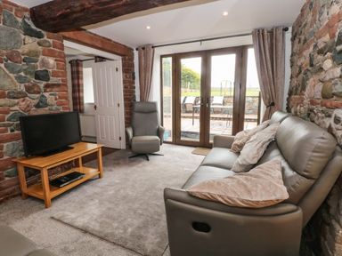A living room with a sofa and armchair facing a television on a wooden stand at Saddleback Barn in Newton Reigny near Penrith