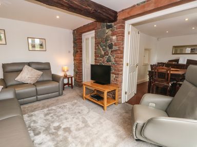 A living room with grey sofas a TV on a wooden stand and a doorway leading to a dining area at Saddleback Barn in Newton Reigny near Penrith