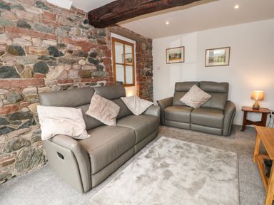 A living room with two gray sofas with cushions a stone wall and a wooden beam at Saddleback Barn in Newton Reigny near Penrith