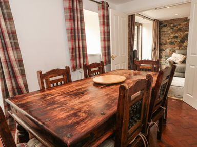 A dining area with a wooden table and chairs and plaid curtains at Saddleback Barn in Newton Reigny near Penrith