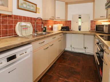 A kitchen with brown tiled backsplash dishwasher sink toaster microwave hotpoint oven and cabinets at Saddleback Barn Newton Reigny near Penrith