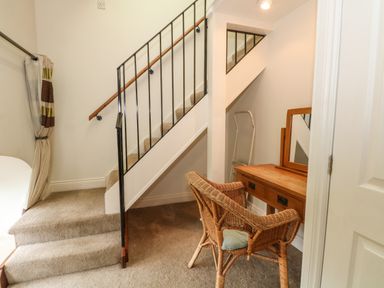 A stairway with carpeted steps and a wooden handrail beside a wooden dressing table with a mirror and a wicker chair at Saddleback Barn in Newton Reigny near Penrith