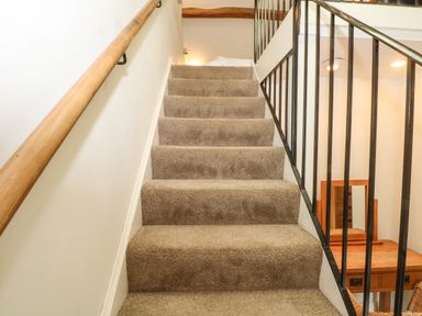 Carpeted stairs with a wooden handrail on the left and black metal railing on the right overlooking a wooden desk with a mirror at Saddleback Barn in Newton Reigny near Penrith