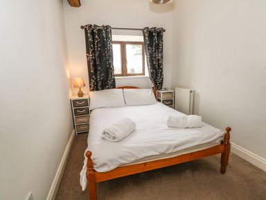 A bedroom with a wooden bed frame white bedding two rolled towels bedside tables with drawers a lamp and a window with dark curtains at Saddleback Barn in Newton Reigny near Penrith