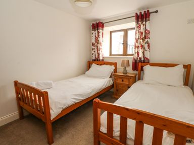 A bedroom with two single beds a wooden nightstand and floral curtains at Saddleback Barn in Newton Reigny near Penrith