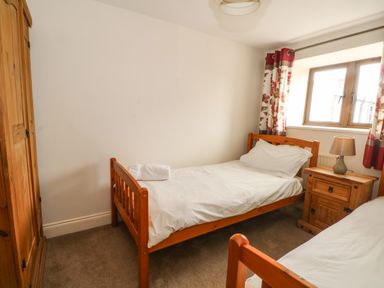 A bedroom with two single wooden beds a wooden wardrobe a nightstand with a lamp and a window with floral curtains at Saddleback Barn in Newton Reigny near Penrith
