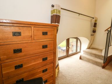 A carpeted area with wooden chest of drawers next to an arched window and small steps with a railing at Saddleback Barn in Newton Reigny near Penrith