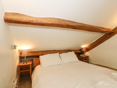 A bedroom with a double bed between two small wooden bedside tables with lamps under a sloped ceiling with exposed wooden beams at Saddleback Barn Newton Reigny near Penrith