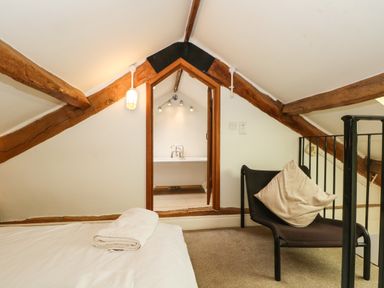 A loft bedroom with a bed with folded towels a chair with a pillow exposed ceiling beams and a doorway leading to a bathroom with a bathtub at Saddleback Barn in Newton Reigny near Penrith