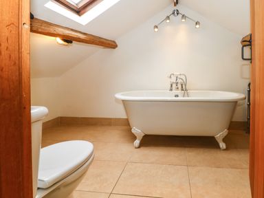A bathroom with a clawfoot bathtub and a toilet under a skylight at Saddleback Barn in Newton Reigny near Penrith