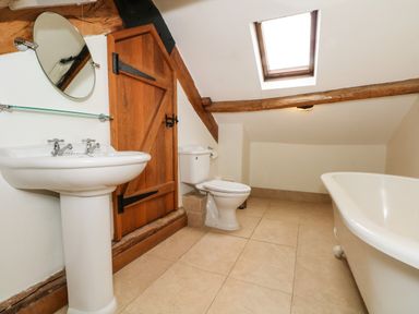 A bathroom with a pedestal sink mirror wooden door toilet and bathtub under a skylight at Saddleback Barn in Newton Reigny near Penrith