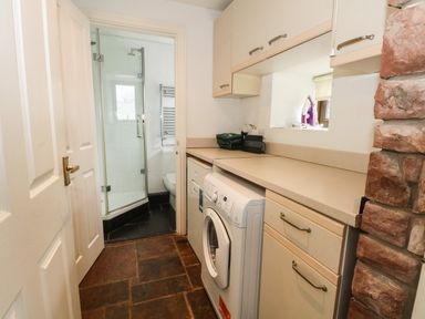 A utility room with a washing machine countertop cabinets and a view into a bathroom with a shower at Saddleback Barn in Newton Reigny near Penrith