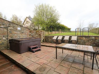 An outdoor patio area with a hot tub table and chairs and sun loungers on a stone tiled floor at Saddleback Barn in Newton Reigny near Penrith