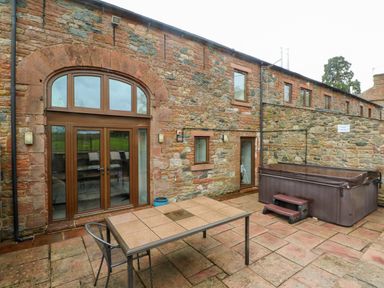 A stone patio with a table, chair, and a covered hot tub outside a stone building at Saddleback Barn in Newton Reigny near Penrith