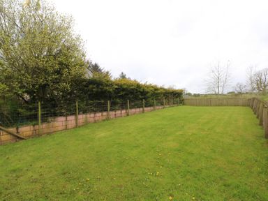 A fenced grass yard with trees and bushes around at Saddleback Barn in Newton Reigny near Penrith
