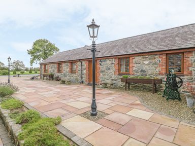 An outdoor view of a stone cottage with a tiled walkway and lamp posts at Lily Cottage in Caeathro near Caernarfon