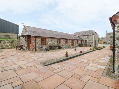 A stone building with a tiled roof and paved courtyard at Lily Cottage in Caeathro near Caernarfon