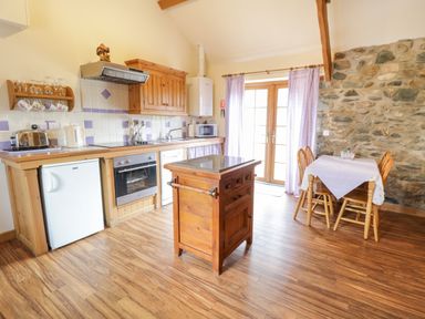 A kitchen with wooden cabinets island and dining table near stone wall at Lavender Cottage in Caeathro near Caernarfon