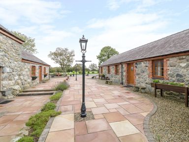 An outdoor stone-paved courtyard with stone buildings flanking both sides and lamp posts in the center at Lavender Cottage in Caeathro near Caernarfon
