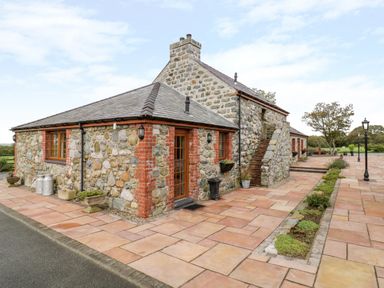 A stone cottage with a tiled roof and outdoor stairs surrounded by a paved patio with planters and lamp posts at Lavender Cottage in Caeathro near Caernarfon
