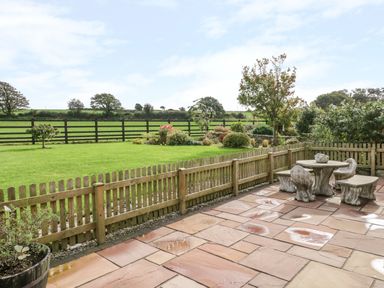 A patio with stone table and chairs next to a wooden fenced garden with trees and shrubs at Lavender Cottage in Caeathro near Caernarfon