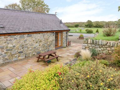 An outdoor patio area with stone walls a wooden picnic table and garden plants at Lavender Cottage in Caeathro near Caernarfon