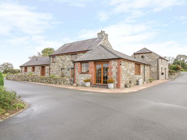 A stone cottage with multiple sections and slate roof surrounded by paved driveway at Lavender Cottage in Caeathro near Caernarfon