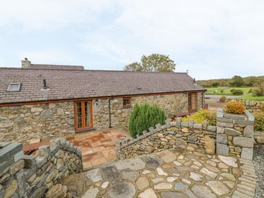 Exterior of a stone cottage with a tiled roof and wooden doors with stone paved patio and garden at Bluebell Cottage in Caeathro near Caernarfon