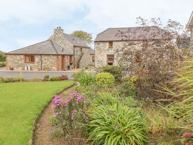 A garden with flowers and shrubs in front of stone cottages at Bluebell Cottage in Caeathro near Caernarfon
