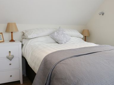 A bedroom with a bed white bedding and a gray throw blanket two bedside tables with lamps and a framed photo at Bicton Lodge in Clun
