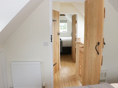 A hallway with wooden doors leading to a bedroom with a window at Bicton Lodge in Clun