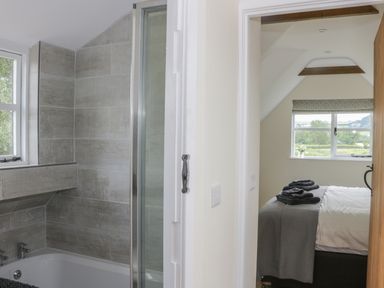 A bathroom with a bathtub and tiled walls next to a bedroom with a bed and a window at Bicton Lodge in Clun