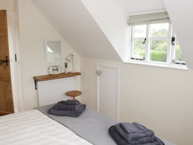 A bedroom with folded towels on a bed a wooden shelf with a lamp and decoration a small stool and a window at Bicton Lodge in Clun
