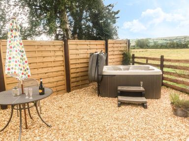 An outdoor area with a hot tub wooden steps a metal table with a bottle and glasses and a closed umbrella at Bicton Lodge in Clun