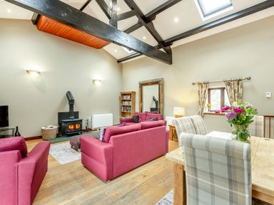 A living room with pink sofas a wood stove a dining table with plaid chairs and flowers at Hill Side Barn in Pennington near Ulverston