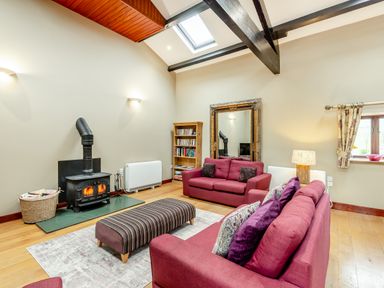 A living room with two red sofas a striped ottoman a wood burning stove bookshelf and a large mirror at Hill Side Barn in Pennington near Ulverston