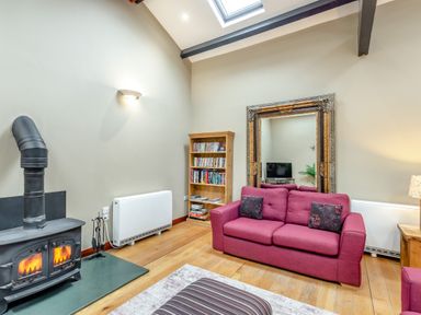 A living room with a pink sofa a wood stove a bookshelf and a large ornate mirror at Hill Side Barn in Pennington near Ulverston