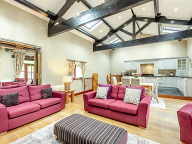 An open living room and kitchen with pink sofas and wooden beams on ceiling at Hill Side Barn in Pennington near Ulverston