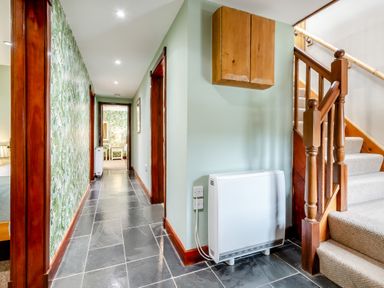 A hallway with a tiled floor wallpaper on one side wooden door frames a staircase with carpet and a heating unit at Hill Side Barn Pennington near Ulverston