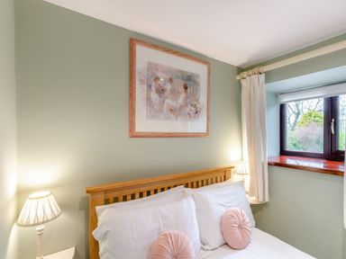 A bedroom with a wooden bed frame pillows and round cushions beside a window with curtains at Hill Side Barn in Pennington near Ulverston