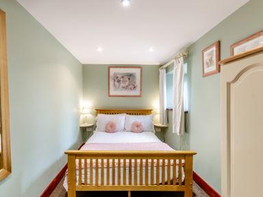 A bedroom with a wooden bed frame white and pink bedding wall art and a wardrobe at Hill Side Barn in Pennington near Ulverston