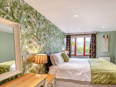 A bedroom with a bed green patterned wallpaper a wooden dresser and a window at Hill Side Barn Pennington near Ulverston