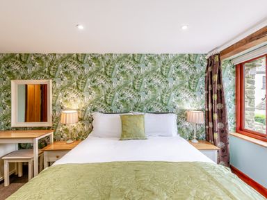 A bedroom with a double bed green bedding tropical wallpaper bedside tables lamps and a window with curtains at Hill Side Barn Pennington near Ulverston