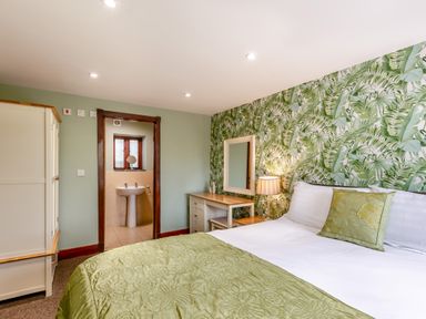 A bedroom with a green bedspread a wardrobe a dressing table bedside lamp and an entrance to a bathroom at Hill Side Barn in Pennington near Ulverston