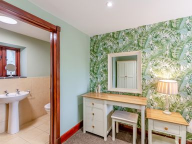A room with a desk stool lamp and mirror next to a bathroom with a sink and toilet at Hill Side Barn in Pennington near Ulverston