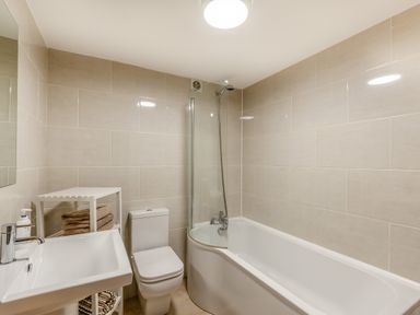 A bathroom with a bathtub shower combination a toilet a sink and shelves with towels at Hill Side Barn in Pennington near Ulverston