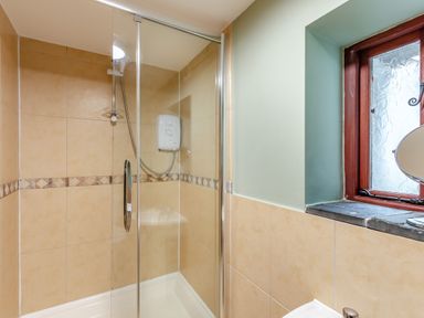 A shower with glass doors beige tiled walls and a small window with frosted glass at Hill Side Barn Pennington near Ulverston