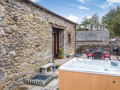 An outdoor patio with a hot tub stone walls benches and a dining table with red cushioned chairs at Hill Side Barn in Pennington near Ulverston