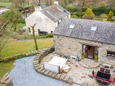 An outdoor patio area with a hot tub surrounded by stone walls and a table with chairs next to a stone house at Hill Side Barn Pennington near Ulverston